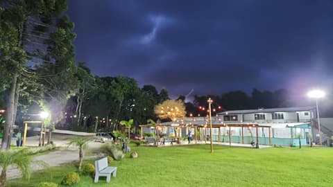 Gramado, pergolados e salão iluminados por varal de luzes à noite na Chácara Primeiro de Maio