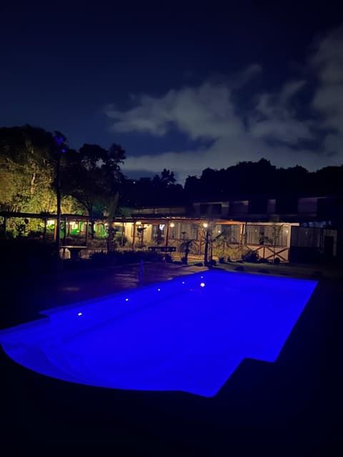 Piscina aquecida com iluminação azul à noite e pergolados iluminados ao fundo