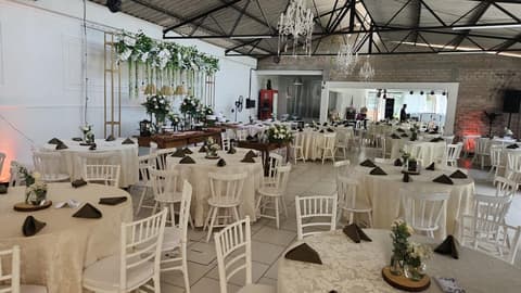 Salão com mesa de bolo, painel de flores e mesas decoradas para recepção de casamento