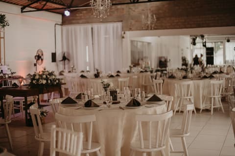 Salão de festas decorado para casamento evangélico com mesas postas, arranjos de flores e lustres
